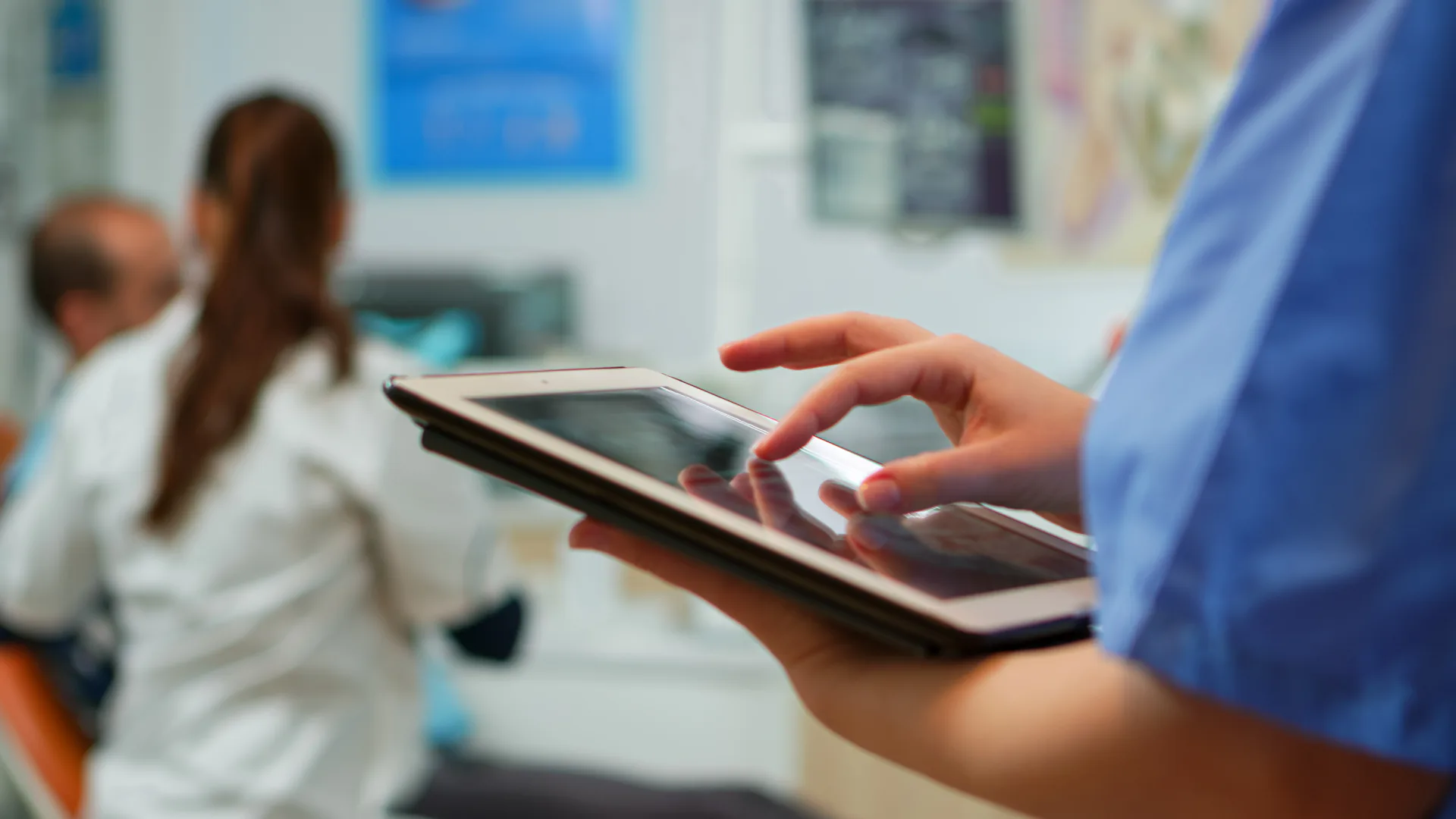 Imagem de um consultório com uma médica atendendo atrás e na frente uma pessoa segurando um tablet - Inteligência Artificial contra fraudes em planos de saúde
