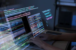 Na imagem, uma tela de computador com códigos de programação e mãos digitando no teclado. 