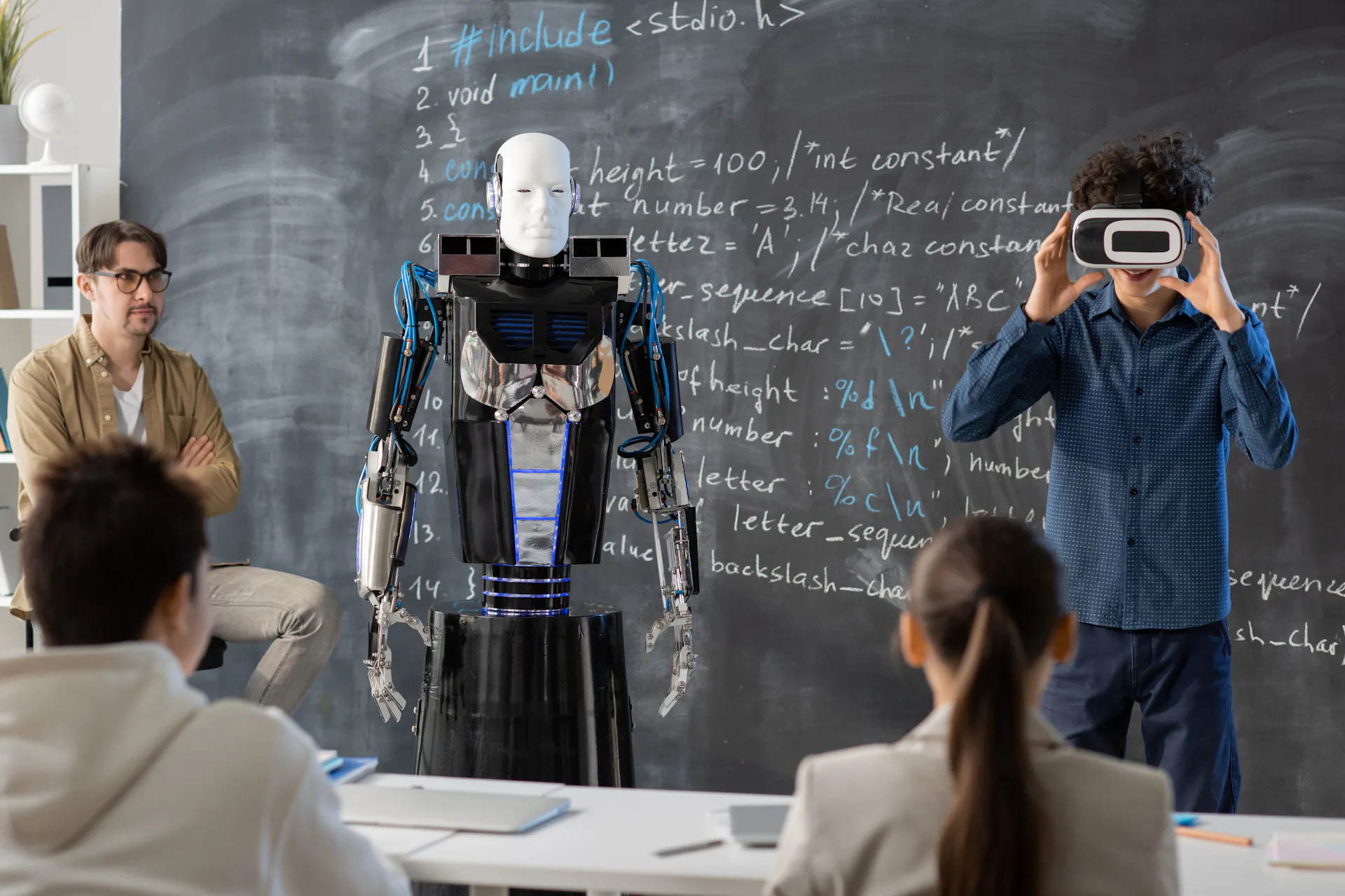 Na imagem, um robô está sendo construído por alunos sob supervisão de um professor.  