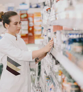 Mulher farmacêutica com jaleco branco na frente de uma prateleira de remédios 