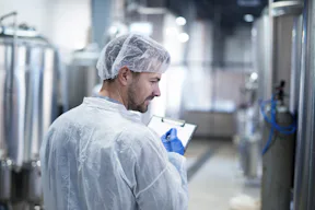 Image of a man inside a food factory, holding a clipboard and validating the products