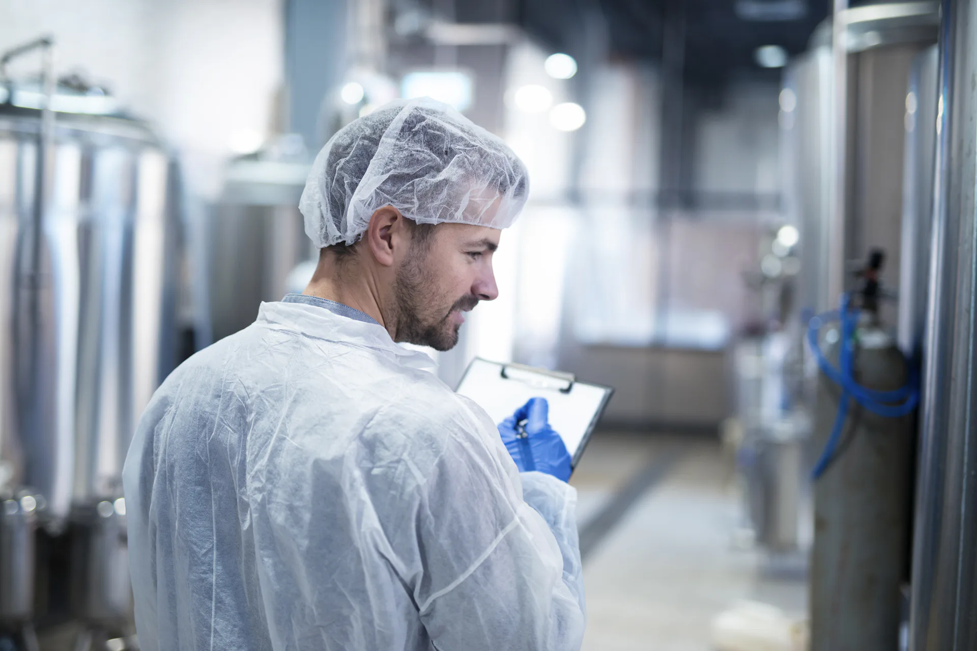 Imagem de um homem dentro de uma fábrica de alimentos, com uma prancheta na mão e validando os produtos 